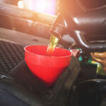 A mechanic pours oil into a vehicle