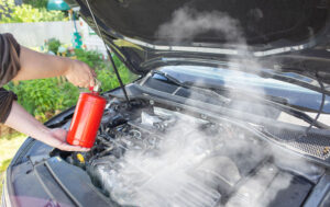 The driver of the car directs a powder fire extinguisher at the engine compartment of the car in which there is fire and smoke.